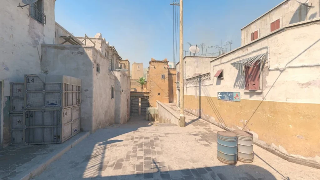 Mapas de CS2: conheça todos os mapas competitivos do Counter-Strike 2 3 Vista de uma rua estreita do mapa Dust II no Counter-Strike 2 (CS2), com arquitetura árabe, paredes desgastadas, barris metálicos e iluminação diurna, cenário clássico para partidas competitivas de FPS.