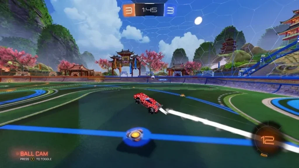 Gameplay de Rocket League em arena temática oriental com carro vermelho acelerando em direção à bola, cenário com templos japoneses, árvores floridas e placar empatado durante partida competitiva.
