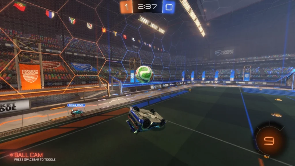 Carro capotado disputa a bola na lateral da arena durante partida de Rocket League, com placar de 1 a 0 e lance competitivo próximo à parede do campo.
